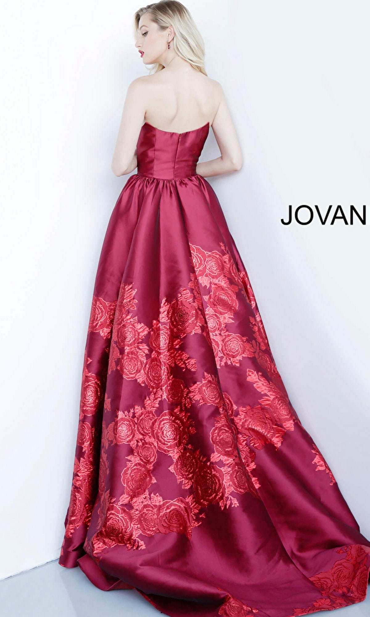 A woman stands with her back to the camera in the Jovani Strapless Floral Long Prom Ball Gown 02038, showing off its elegant A-line silhouette against a white background. The word